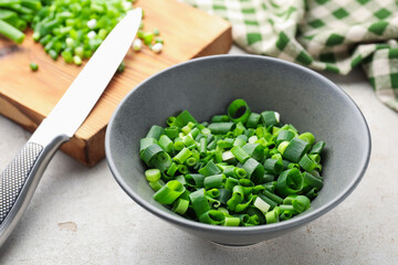 Bowl with cut green onions on light grey table, closeup