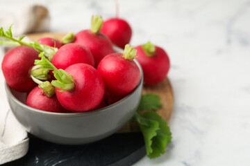 Fresh radishes in bowl on white marble table, closeup. Space for text