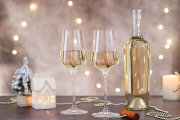 Glasses of white wine and Christmas decor on grey table against background with blurred lights
