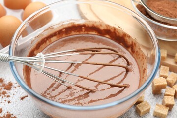 Chocolate dough with whisk in bowl and ingredients on grey textured table, closeup