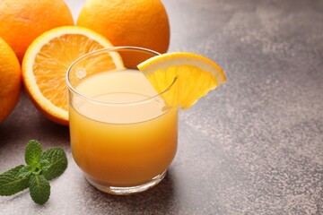 Fresh orange juice in glass, mint and fruits on grey table, closeup. Space for text