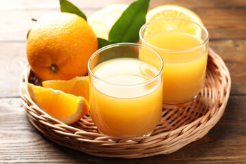 Fresh orange juice, fruits and green leaves on wooden table, closeup
