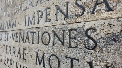 Rome, Italy - 12 January 2025. Detail from the Res Gestae at the Ara Pacis focusing on etched Latin text in stone, highlighting the word "VENATIONES" with weathered surface.