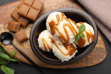 Tasty ice cream with caramel sauce and mint in bowl on black table, flat lay