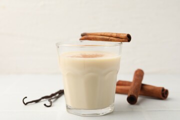 Delicious protein shake in glass, cinnamon and vanilla pods on white table, closeup