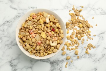 Tasty granola with dried fruits and nuts in bowl on white marble table, flat lay