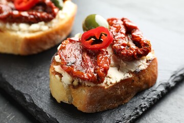 Delicious bruschettas with cream cheese, sun-dried tomatoes, chili pepper and green olives on table, closeup