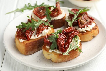 Delicious bruschettas with cream cheese, sun-dried tomatoes and arugula on white wooden table, closeup
