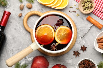 Tasty mulled wine in pot, ingredients and corkscrew on gray textured table, flat lay