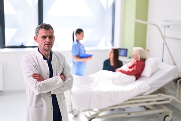 Obraz premium Doctor standing confidently in a hospital room while nurses attend to a patient in bed