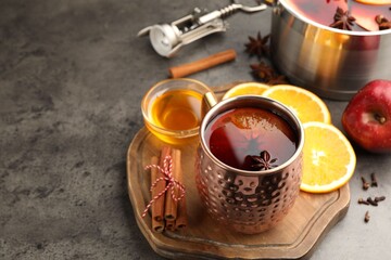 Tasty mulled wine in mug and ingredients on gray textured table, closeup. Space for text
