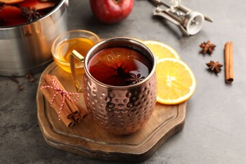 Tasty mulled wine in mug and ingredients on gray textured table, closeup