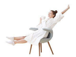 Relaxed young woman in a white bathrobe sitting comfortably, stretching and holding a cup of hot...