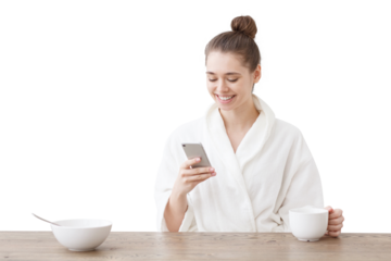 Smiling woman in a bathrobe checking her mobile phone with calorie tracker app while enjoying a healthy breakfast