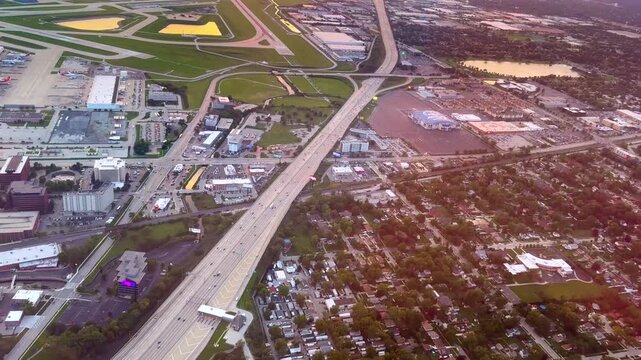 Scenic aerial view of highway traffic flowing past airport in cityscape at sunset. Breathtaking moving view from aircraft.