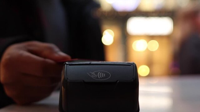 Close up of hand tapping a credit card on a contactless pos terminal at checkout in a retail store, soft bokeh background emphasizing nfc wireless payment transaction