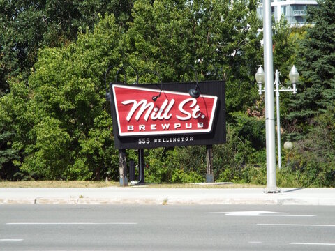 Ottawa,ON, Canada-June 29,2025: A large, black and red angled sign for the "Mill St. Brewpub" is mounted near a street. The address 555 WELLINGTON is noted below the main text.
