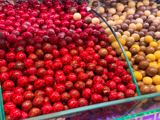 Sugar and chocolate coated berry candies filling a curved glass container in bazaar Istanbul. Decorative sweets, festive indulgence, and colorful confectionery presentation emphasized through shine