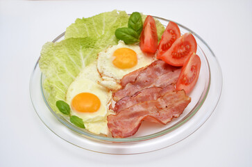 A hearty breakfast on a plate of scrambled eggs with bacon, tomatoes and herbs