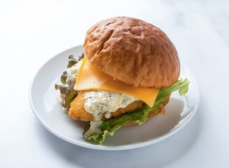 Delicious fish sandwich with cheese and sauce on a plate