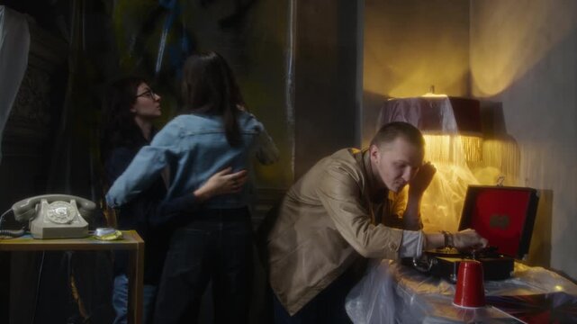 Medium shot of young people partying in abandoned house with two women dancing to old record player music, copy space