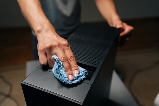 Cropped shot of technician male cleaning computer case with blue microfiber cloth, ensuring dust and debris removed for optimal performance in dark workshop. Concept of service, cleaning desktop PC.