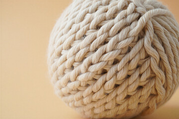 Knitted 3D shape single ball of light beige natural yarn with visible fibers rests on a neutral surface.