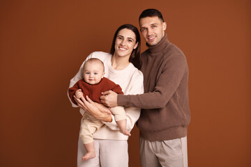 Happy parents with their cute baby on brown background