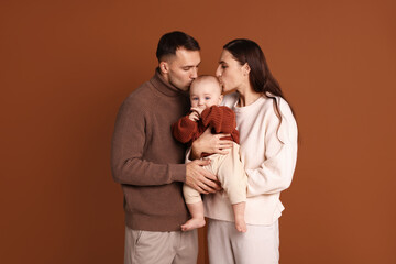 Parents kissing their cute baby on brown background