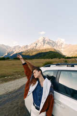 Woman by white car near mountain range on roadside, travel and roadtrip scene with adventure spirit and freedom, casual jacket, scenic landscape and outdoor exploration.