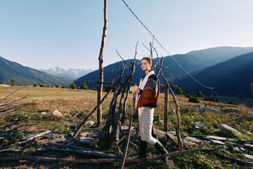 Naklejka premium woman mountains field cup sweater rural nature standing by a rustic stick fence in an alpine valley, cozy jacket and boots enjoying morning sunlight and scenic mountain landscape