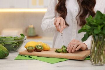 Woman cutting kiwi for blending at white marble table indoors, closeup