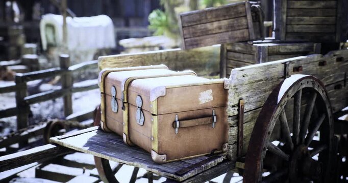 A weathered wooden cart displays two vintage suitcases in a rural area. Surrounding elements hint at a bygone era, creating a nostalgic atmosphere filled with history and charm.