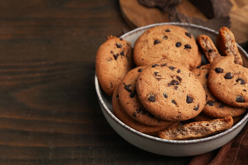 Yummy chocolate chip cookies in bowl on wooden table, closeup. Space for text