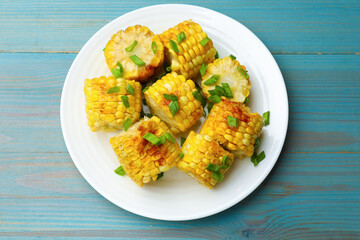 Pieces of grilled corn cobs with green onions on blue wooden table, top view