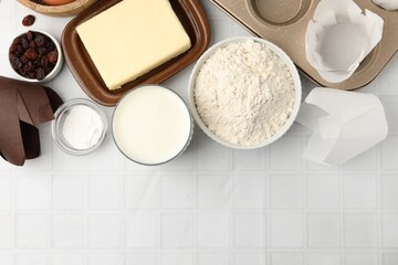 Ingredients for making muffins and cupcake tray on white tiled table, flat lay. Space for text