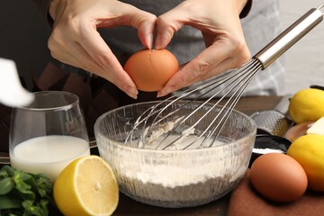 Making muffins. Woman cracking egg into dough at table, closeup
