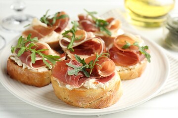 Delicious bruschettas with cream cheese, prosciutto and arugula on table, closeup