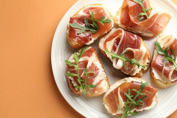 Delicious bruschettas with cream cheese, prosciutto and arugula on orange table, top view. Space for text