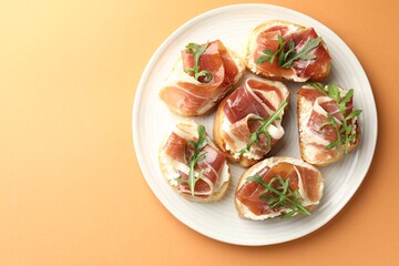 Delicious bruschettas with cream cheese, prosciutto and arugula on orange table, top view. Space for text