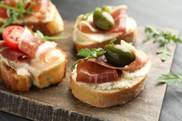 Delicious bruschettas with cream cheese, prosciutto, green olives, tomatoes and arugula on table, closeup