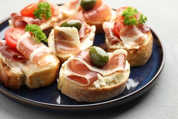 Delicious bruschettas with cream cheese, prosciutto, green olives, tomatoes and parsley on table, closeup