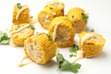 Pieces of boiled corn cobs with parsley and sauce on white table, closeup