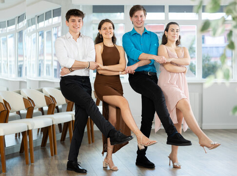 Group of enthusiastic cheerful young guys and girl traditionally lined in row while performing Greek sirtaki during dance class in sunny studio..