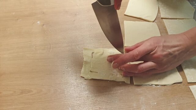 Slow motion footage of a woman cutting puff pastry in wrapping a pineapple wedge on it. Food