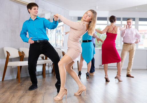 Positive adult woman enjoying active dances with young male partner in modern dance studio, practicing playful jitterbug moves..