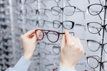 Hands choosing eyeglass frames at optician store eyewear shopping and vision care