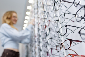Eyeglass frames on optical store display with customer browsing in background