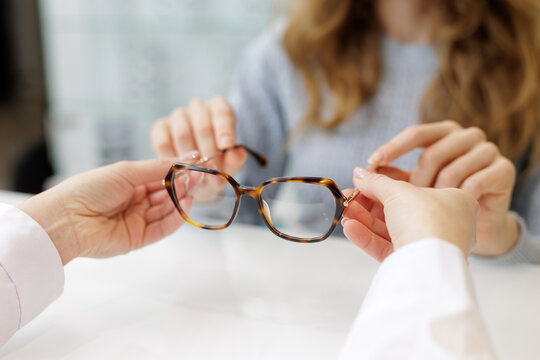 Optician showing eyeglass frame to customer at counter during prescription eyewear fitting