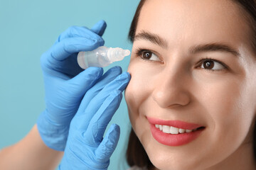 Doctor's hands with eye drops and woman on blue background, closeup